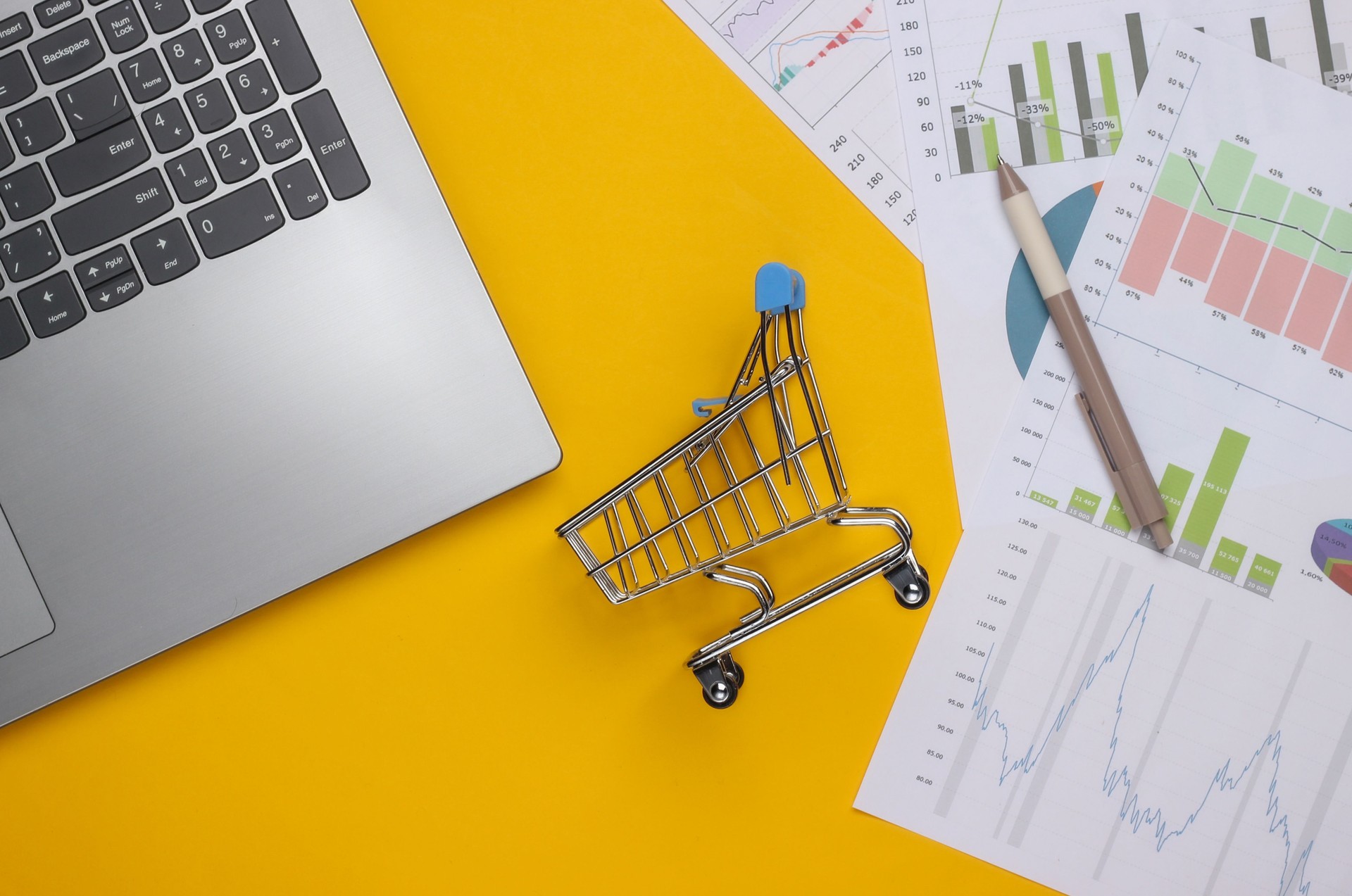 Laptop, shopping trolley with graphs and charts on a yellow background. Business plan, financial analytics, statistics. Top view